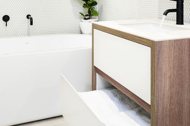 Foto de cuarto de baño contemporáneo pequeño con puertas de armario de madera en tonos medios, bañera exenta, baldosas y/o azulejos blancos, paredes blancas, lavabo integrado, suelo gris y encimeras blancas