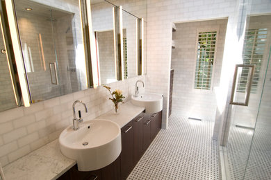 Imagen de cuarto de baño actual con armarios con paneles lisos, puertas de armario de madera en tonos medios, encimera de mármol, baldosas y/o azulejos blancos, losas de piedra y lavabo sobreencimera
