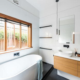 This is an example of a mid-sized modern master bathroom in Melbourne with flat-panel cabinets, a freestanding tub, white tile, ceramic tile, white walls, a vessel sink, engineered quartz benchtops, black floor, medium wood cabinets, a corner shower, a hinged shower door and white benchtops.