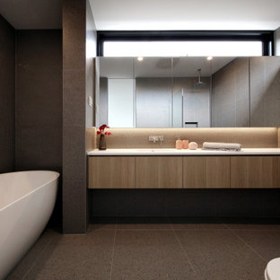 This is an example of a contemporary bathroom in Melbourne with flat-panel cabinets, medium wood cabinets, a freestanding tub, gray tile, grey floor and white benchtops.