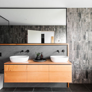 This is an example of a contemporary master bathroom in Hobart with flat-panel cabinets, medium wood cabinets, a freestanding tub, a one-piece toilet, gray tile, grey walls, a vessel sink, wood benchtops, grey floor, brown benchtops, a double vanity and a floating vanity.