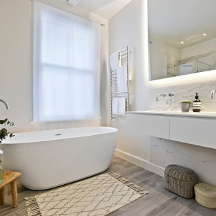This is an example of a medium sized contemporary ensuite bathroom in Other with flat-panel cabinets, white cabinets, a freestanding bath, marble tiles, white walls, a wall-mounted sink, grey floors, black and white tiles and white worktops.