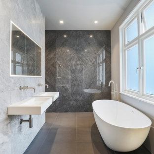 Inspiration for a contemporary ensuite bathroom in London with open cabinets, a freestanding bath, a built-in shower, grey tiles, a wall-mounted sink, grey floors, an open shower and white worktops.