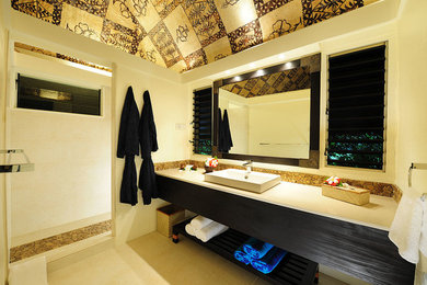 Esempio di una stanza da bagno tropicale con lavabo a bacinella, ante lisce, ante nere, doccia alcova e piastrelle beige