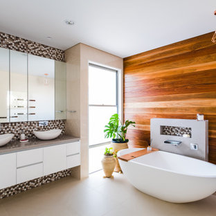Photo of a contemporary bathroom in Gold Coast - Tweed with flat-panel cabinets, white cabinets, a freestanding tub, multi-coloured tile, mosaic tile, brown walls, a vessel sink, beige floor, grey benchtops, a niche, a double vanity, a floating vanity and wood walls.
