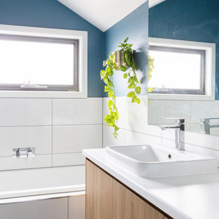 This is an example of a contemporary bathroom in Melbourne with flat-panel cabinets, medium wood cabinets, an alcove tub, white tile, blue walls, a drop-in sink, black floor, white benchtops, a floating vanity and vaulted.