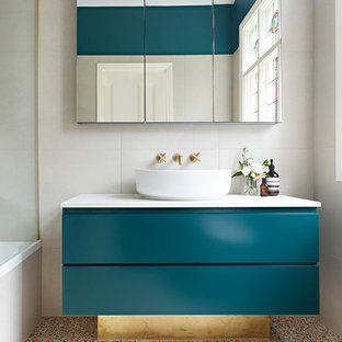 Small contemporary master bathroom in Melbourne with beige tile, beige walls, terrazzo floors, a vessel sink, multi-coloured floor, white benchtops, green cabinets, a shower/bathtub combo, a hinged shower door, furniture-like cabinets, a drop-in tub, a wall-mount toilet, stone tile and engineered quartz benchtops.
