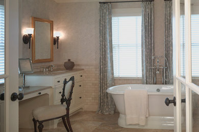Klassisk inredning av ett badrum, med ett undermonterad handfat, vita skåp, ett fristående badkar, beige kakel och tunnelbanekakel