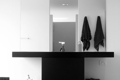 Réalisation d'une salle de bain design avec des portes de placard noires, un carrelage noir et un plan de toilette en surface solide.