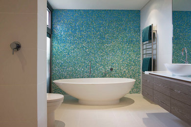 Cette photo montre une salle de bain principale tendance en bois clair avec un placard à porte plane, une baignoire indépendante, WC à poser, un carrelage bleu, mosaïque, un mur bleu, un sol en carrelage de céramique, une vasque et un plan de toilette en surface solide.