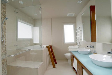 Example of a mid-sized beach style master ceramic tile ceramic tile and white floor bathroom design in Vancouver with flat-panel cabinets, medium tone wood cabinets, a one-piece toilet, white walls, a vessel sink, solid surface countertops and a hinged shower door