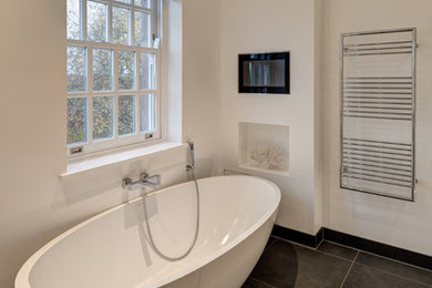 Photo of a large modern ensuite bathroom in London with flat-panel cabinets, black cabinets, a freestanding bath, grey tiles, porcelain tiles, white walls, porcelain flooring, an integrated sink and solid surface worktops.