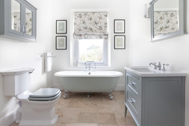 Inspiration for a medium sized classic bathroom in Gloucestershire with shaker cabinets, grey cabinets, a one-piece toilet, ceramic tiles, white walls, limestone flooring, a claw-foot bath, beige tiles, a console sink and beige floors.