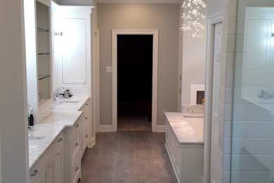 Example of a large trendy master white tile and subway tile porcelain tile and brown floor bathroom design in New Orleans with recessed-panel cabinets, white cabinets, an undermount tub, gray walls, an undermount sink and marble countertops