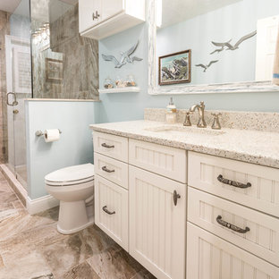 This is an example of a large beach style 3/4 bathroom in Other with beaded inset cabinets, white cabinets, a corner shower, beige tile, porcelain tile, blue walls, porcelain floors, an undermount sink, recycled glass benchtops, beige floor and a hinged shower door.
