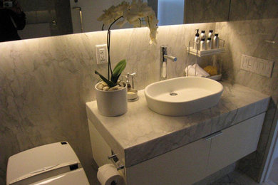 トロントにある中くらいなおしゃれなバスルーム (浴槽なし) (ベッセル式洗面器、フラットパネル扉のキャビネット、白いキャビネット、大理石の洗面台、一体型トイレ	、白い壁) の写真
