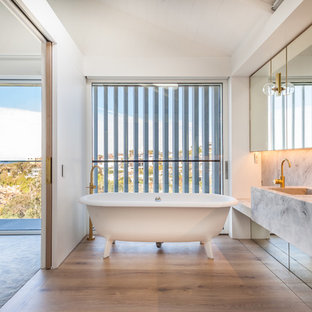 Contemporary bathroom in Sydney with a freestanding tub, white walls, medium hardwood floors, an integrated sink, brown floor and grey benchtops.
