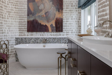 Klassisches Badezimmer mit flächenbündigen Schrankfronten, dunklen Holzschränken, freistehender Badewanne, beiger Wandfarbe, Einbauwaschbecken, grauem Boden, weißer Waschtischplatte und Tapetenwänden