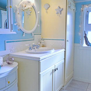 Foto di una piccola stanza da bagno con doccia stile marino con ante con riquadro incassato, ante gialle, piastrelle bianche, piastrelle in ceramica, pareti blu, pavimento in vinile, lavabo da incasso, top piastrellato e pavimento beige