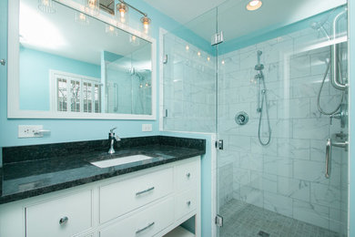 Corner shower - small modern master gray tile and porcelain tile porcelain tile and gray floor corner shower idea in Other with recessed-panel cabinets, white cabinets, a two-piece toilet, blue walls, an undermount sink, granite countertops, a hinged shower door and black countertops