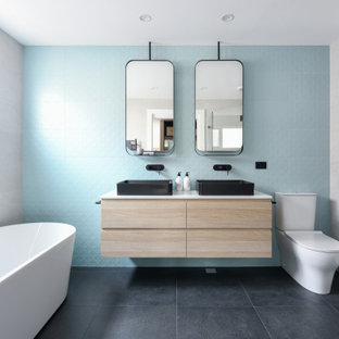 Photo of a mid-sized contemporary bathroom in Sydney with flat-panel cabinets, light wood cabinets, a freestanding tub, a two-piece toilet, blue tile, white tile, a vessel sink, black floor, white benchtops, a double vanity and a floating vanity.