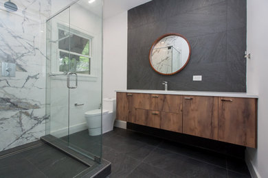 Contemporary bathroom in Dallas with flat-panel cabinets, dark wood cabinets, a corner shower, a one-piece toilet, black tiles, porcelain tiles, white walls, porcelain flooring, a submerged sink, engineered stone worktops, black floors, a hinged door, white worktops, a single sink and a floating vanity unit.