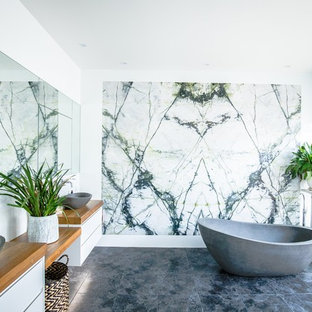 This is an example of a contemporary bathroom in Sydney with flat-panel cabinets, white cabinets, a freestanding tub, white walls, a vessel sink, wood benchtops, black floor and brown benchtops.