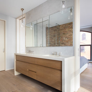 Inspiration for a contemporary master light wood floor and brown floor walk-in shower remodel in New York with flat-panel cabinets, medium tone wood cabinets, gray walls, an integrated sink, a hinged shower door and white countertops