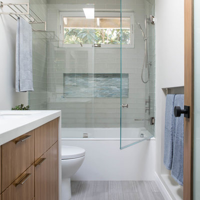 Trendy 3/4 glass tile porcelain tile and gray floor bathroom photo in Los Angeles with flat-panel cabinets, medium tone wood cabinets, a one-piece toilet, an undermount sink, quartz countertops, a hinged shower door and white countertops