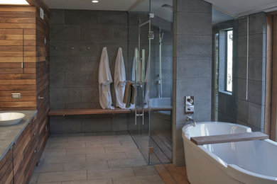 Expansive contemporary ensuite bathroom in Orange County with a vessel sink, medium wood cabinets, soapstone worktops, a freestanding bath, a built-in shower, a two-piece toilet, grey tiles, stone tiles and grey walls.