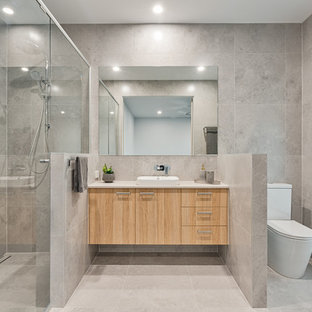 Photo of a contemporary 3/4 bathroom in Sunshine Coast with flat-panel cabinets, light wood cabinets, an alcove shower, a two-piece toilet, gray tile, a drop-in sink, grey floor and white benchtops.