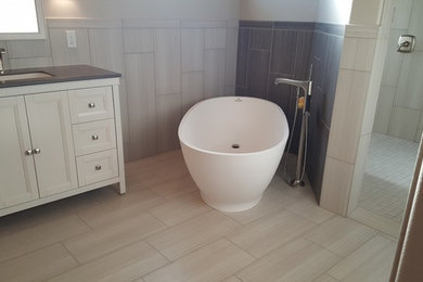 Example of a minimalist master gray tile and porcelain tile porcelain tile and gray floor bathroom design in Other with furniture-like cabinets, white cabinets, a two-piece toilet, white walls, an undermount sink and solid surface countertops