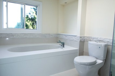 Large minimalist white tile bathroom photo in Toronto with solid surface countertops and an undermount tub