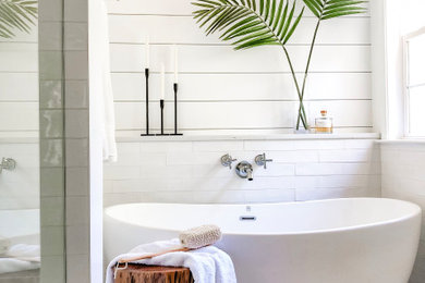 Photo of a medium sized coastal ensuite bathroom in Charlotte with a freestanding bath, an alcove shower, a two-piece toilet, white tiles, porcelain tiles, white walls, porcelain flooring, a submerged sink, engineered stone worktops, beige floors, white worktops, double sinks, tongue and groove walls, flat-panel cabinets, distressed cabinets, a hinged door and a built in vanity unit.