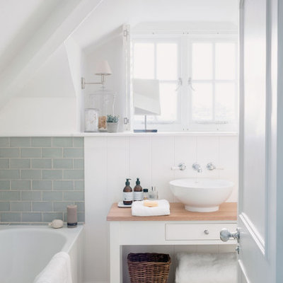 Small beach style master green tile and subway tile pebble tile floor and beige floor alcove bathtub photo in Cornwall with white walls, wood countertops, brown countertops, furniture-like cabinets, white cabinets and a vessel sink