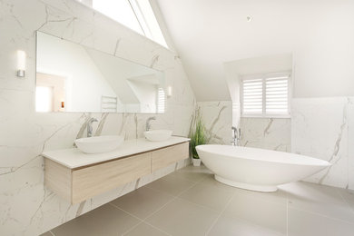 Klassisches Badezimmer En Suite mit flächenbündigen Schrankfronten, hellen Holzschränken, freistehender Badewanne, weißen Fliesen, Keramikfliesen, gelber Wandfarbe, Keramikboden, Quarzit-Waschtisch, grauem Boden und weißer Waschtischplatte in Gloucestershire