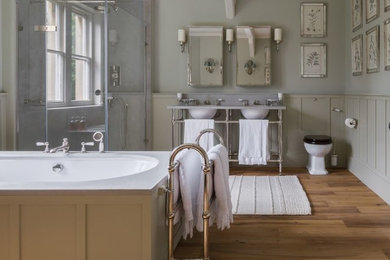 Inspiration for a large classic family bathroom in London with shaker cabinets, green cabinets, a freestanding bath, a corner shower, a one-piece toilet, green walls, medium hardwood flooring, a console sink, marble worktops, brown floors, a hinged door and white worktops.