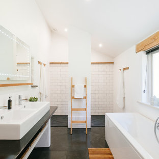 This is an example of a rural ensuite bathroom in Cornwall with a freestanding bath, a built-in shower, white tiles, white walls, a vessel sink, grey floors, an open shower and black worktops.
