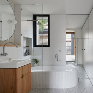 This is an example of a mid-sized contemporary 3/4 bathroom in Melbourne with flat-panel cabinets, medium wood cabinets, a drop-in tub, a shower/bathtub combo, a one-piece toilet, white tile, porcelain tile, white walls, an open shower, a console sink, grey floor and white benchtops.