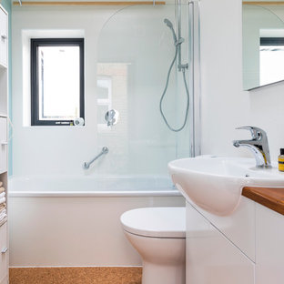 Small contemporary kids bathroom in London with flat-panel cabinets, white cabinets, an alcove tub, an alcove shower, a one-piece toilet, glass sheet wall, white walls, cork floors, a drop-in sink, wood benchtops, brown floor, a hinged shower door and brown benchtops.