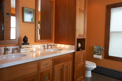 Example of a mid-sized arts and crafts 3/4 porcelain tile and gray floor drop-in bathtub design in Milwaukee with shaker cabinets, medium tone wood cabinets, a two-piece toilet, orange walls, an undermount sink and quartzite countertops