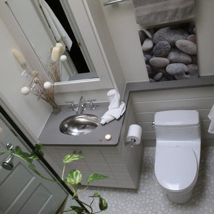 Modern inredning av ett mellanstort en-suite badrum, med möbel-liknande, grå skåp, en toalettstol med hel cisternkåpa, grå väggar, klinkergolv i småsten, ett undermonterad handfat, bänkskiva i rostfritt stål och en dusch i en alkov