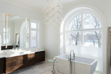 Modelo de cuarto de baño clásico renovado con lavabo sobreencimera, armarios con paneles empotrados, puertas de armario de madera en tonos medios, bañera exenta, paredes blancas y suelo de mármol