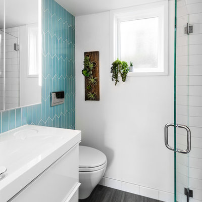 Example of a small trendy 3/4 blue tile and ceramic tile gray floor alcove shower design in Seattle with flat-panel cabinets, white cabinets, a wall-mount toilet, white walls, an integrated sink, solid surface countertops, a hinged shower door and white countertops
