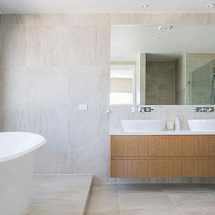 Exempel på ett stort minimalistiskt vit vitt en-suite badrum, med möbel-liknande, skåp i ljust trä, ett fristående badkar, en öppen dusch, en toalettstol med hel cisternkåpa, beige kakel, porslinskakel, beige väggar, kalkstensgolv, ett fristående handfat, bänkskiva i kvarts, beiget golv och med dusch som är öppen