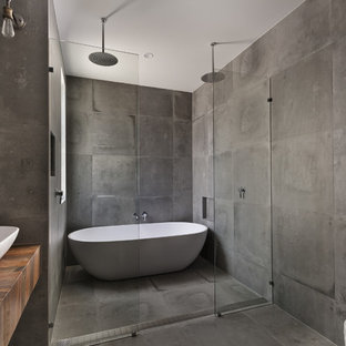 Inspiration for a large industrial master gray tile concrete floor bathroom remodel in San Diego with gray walls, a vessel sink, wood countertops, open cabinets, medium tone wood cabinets, a wall-mount toilet and brown countertops