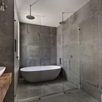 Inspiration for a large industrial master gray tile concrete floor bathroom remodel in San Diego with gray walls, a vessel sink, wood countertops, open cabinets, medium tone wood cabinets, a wall-mount toilet and brown countertops