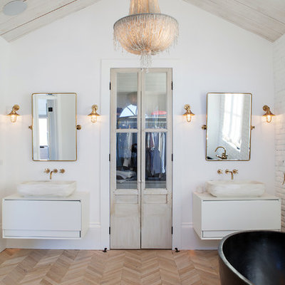 Inspiration for a mid-sized country master white tile light wood floor and beige floor freestanding bathtub remodel in Orange County with flat-panel cabinets, white cabinets, white walls, a vessel sink and solid surface countertops