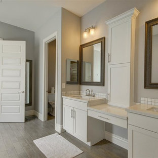 Immagine di una stanza da bagno padronale stile americano di medie dimensioni con ante in stile shaker, ante bianche, WC monopezzo, piastrelle bianche, piastrelle a mosaico, pareti grigie, pavimento in compensato, lavabo sottopiano e top piastrellato