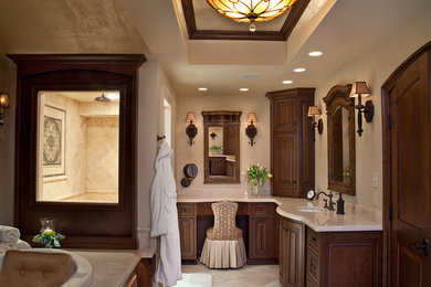 Diseño de cuarto de baño principal clásico con armarios con paneles empotrados, puertas de armario de madera en tonos medios, paredes beige, suelo de travertino y lavabo integrado